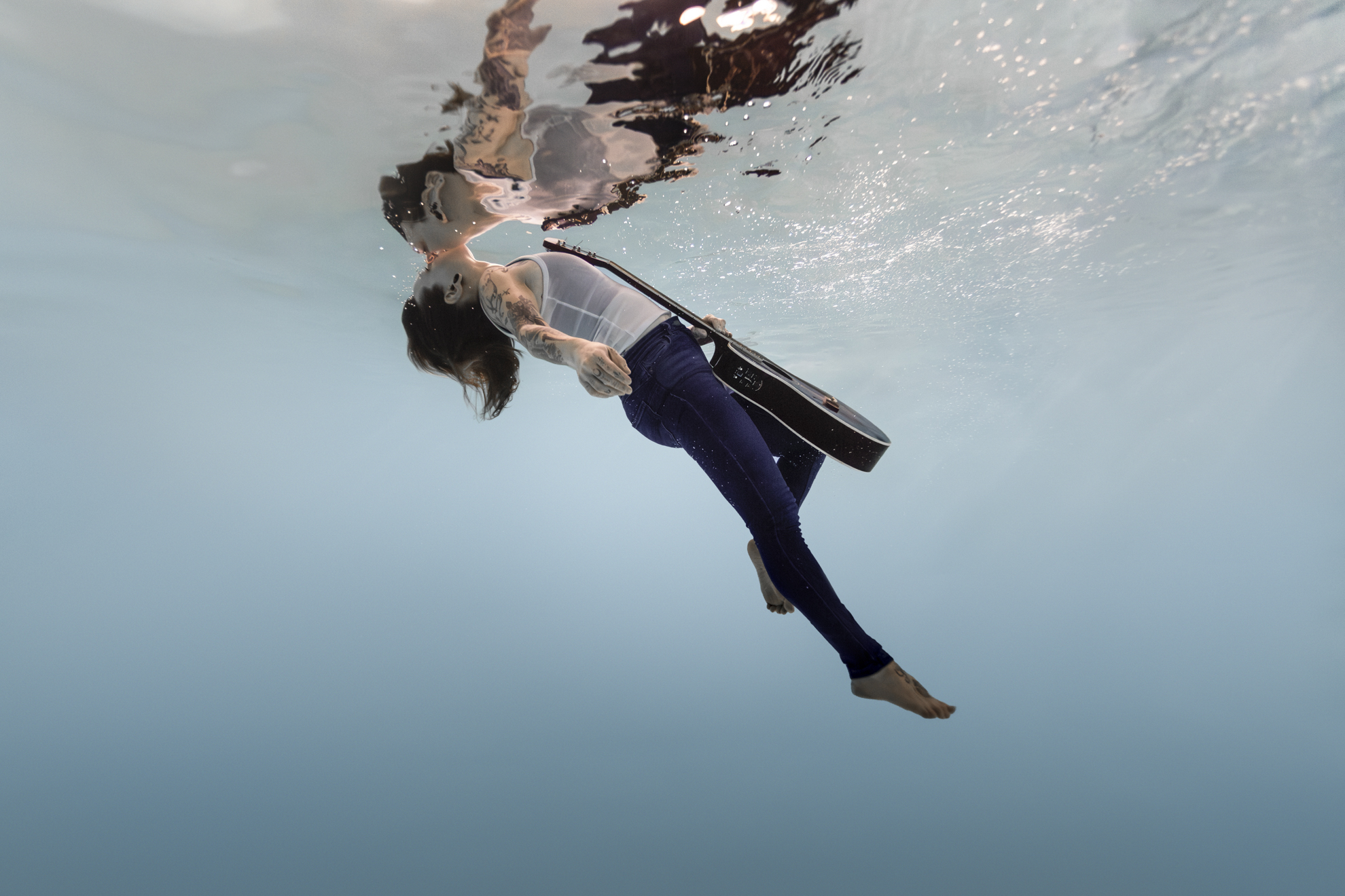 Portrait sous l’eau d’une femme musicienne avec guitare en suspension dans une séance photo aquatique