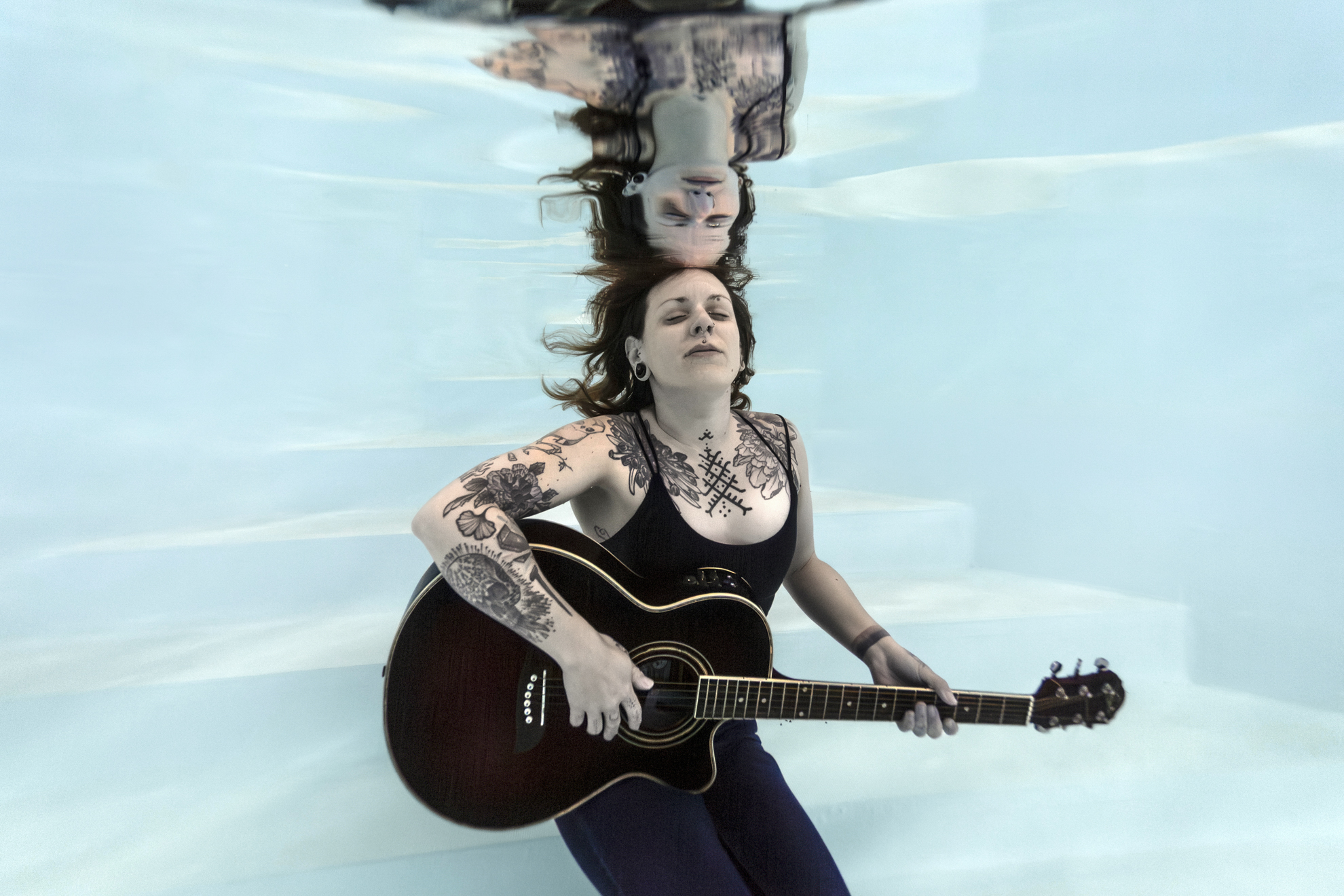 Scène poétique sous l’eau avec une femme flottant et tenant une guitare lors d’un shooting aquatique